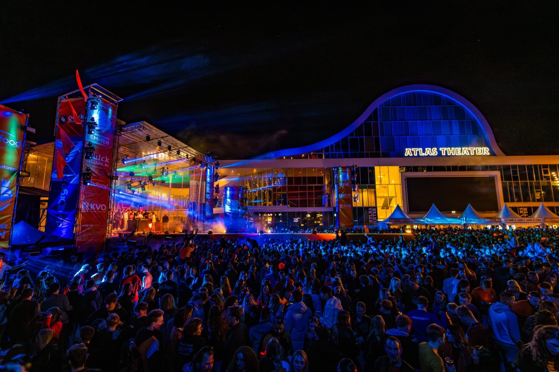 Het Atlas Theater blauw uitgelicht boven een vol plein in de avond