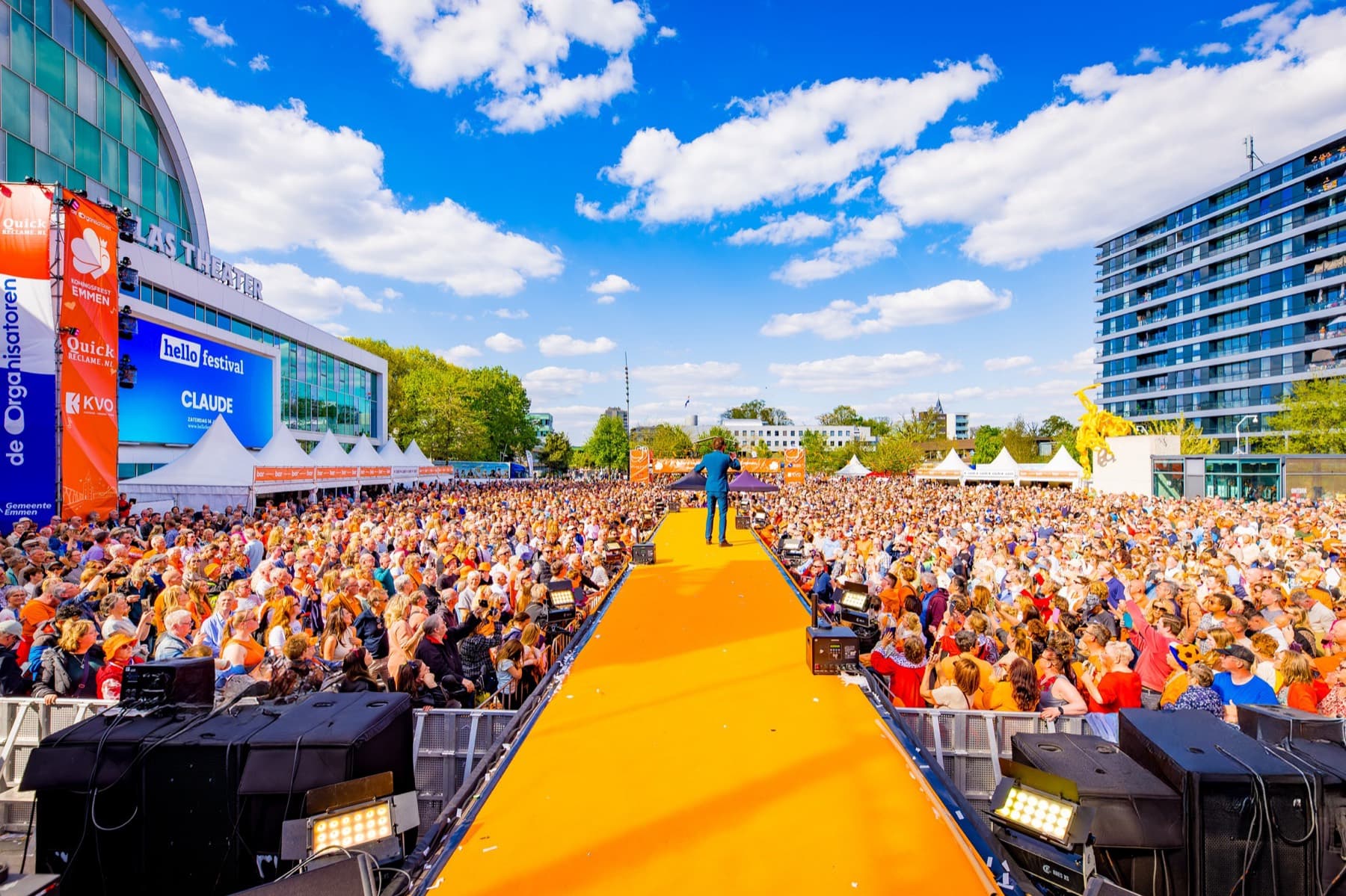 Het Raadhuisplein in Emmen tijdens Koningsdag: de oranje loopbrug dwars door een volgepakt plein, met het Atlas Theater op de achtergrond