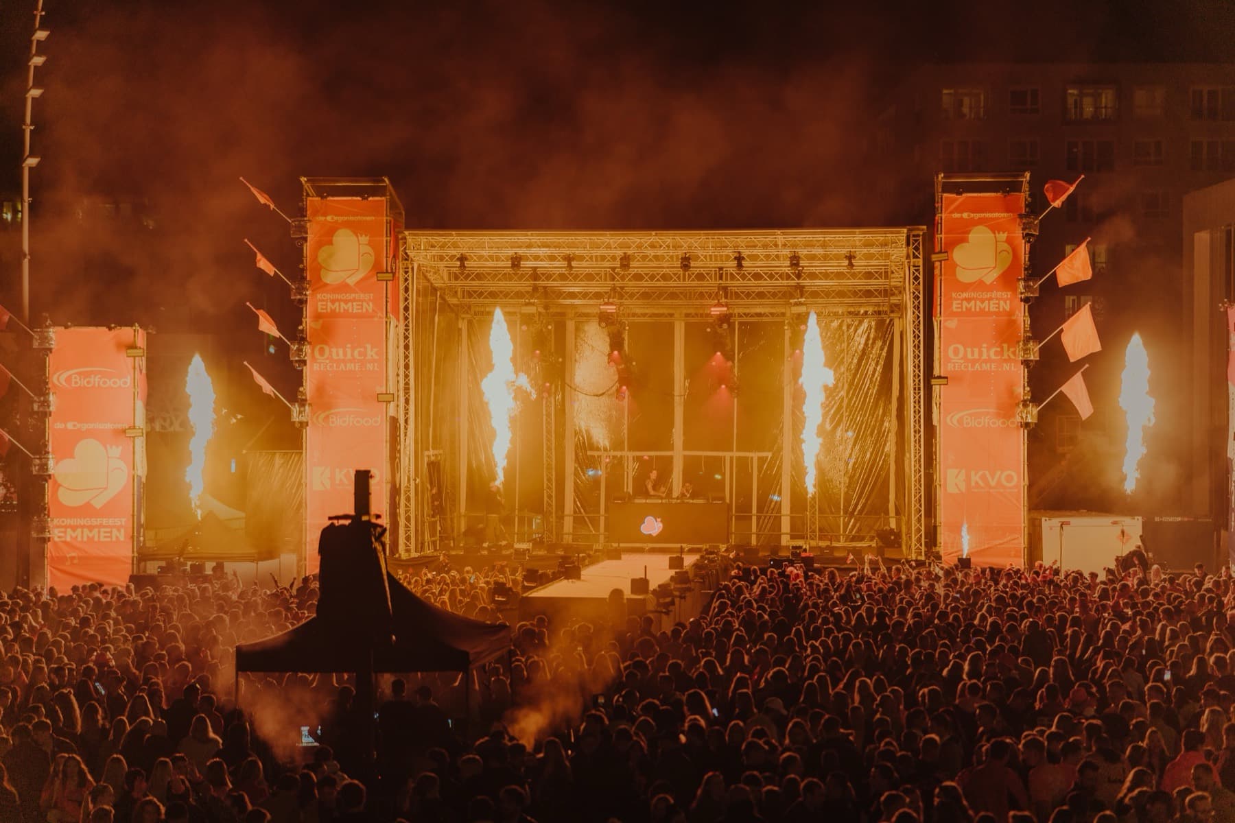 Het hoofdpodium in oranje rook boven een volle bak, laat op de avond